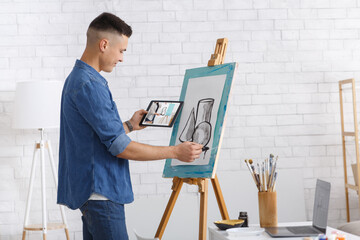 Art lesson online and hobbies during coronavirus quarantine at home. Young man draws picture, holds...