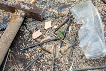 Old vintage hammer, wood saw, nails, safety glasses and sawdust on a wooden background, close-up, selective focus.