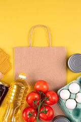 Naklejka na ściany i meble Food donations on yellow background with copyspace - pasta, fresh vegatables, canned food, baguette, eggs, oil. Donation, volunteering, contactless delivery food concept, vertical composition. Mockup