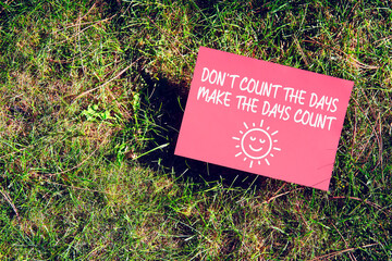 Inspirational message of Don't Count The Days, Make The Days Count on paper on grass in nature. Being productive and making most of the life concept.