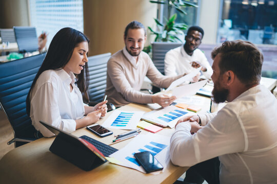 Group of successful male and female colleagues discussing revenue monetary gain during collaboration work on paper financial reports, diverse employees brainstorming at table desk with touch pad