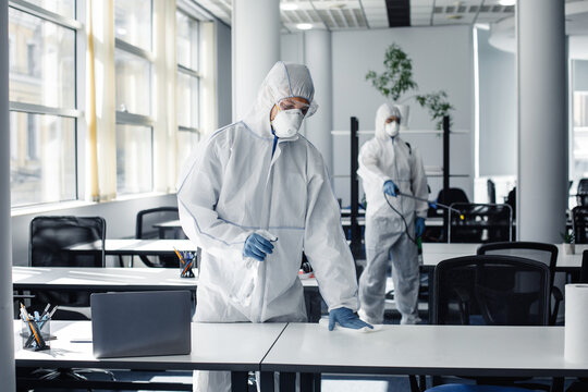 People in hazmat, protective mask and glasses making disinfection of furniture in office with chemicals during coronavirus quarantine