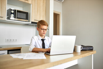 young caucasian business boy work from home using laptop, he is in formal wear, suit, in eyeglasses. intelligent boy is pretend to be adult