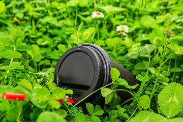 A black paper coffee cup with a red straw is thrown into the green grass. Environmental pollution with household waste