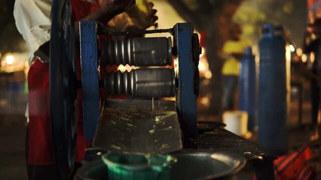 A Black African Man squeezes a sugar cane at Forodhani Night Street Market to make fresh, organic juice with a hand powered juicer. Healthy product from a Zanzibar Street Vendor