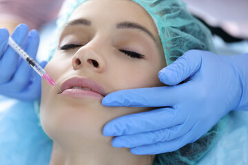 Beautician in rubber gloves makes collagen injection into lips of young woman. Aesthetic medicine lip augmentation concept.