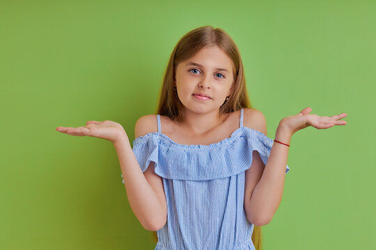 astonished worried teengirl is impressed by unbelievable news dont know, she cant solve decide choose, shrug shoulders isolated on green background dressed in summer dress