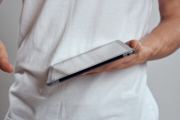 Tablet with a touch screen on a light background male hands white t-shirt cropped view