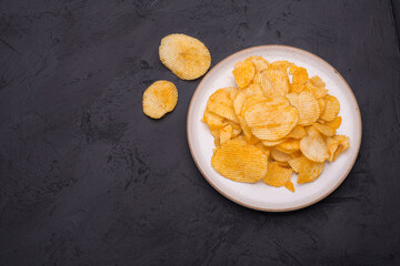 Crispy potato chips in bowl on dark table