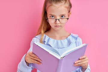 adorable caucasian girl in eyeglasses read a book isolated, smart intelligent child love learning, studying, keen on education