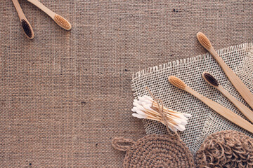 Natural bathroom tools, sustainable zero waste and lifestyle concept. Wooden toothbrushes, bamboo swabs, and handmade jute body washclothes on fabric background with copy space, mockup