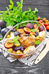 Chicken with fruits and tomatoes in glass pan on dark board