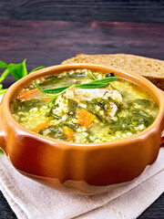 Soup with couscous and spinach in clay bowl on dark board