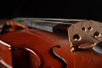 Details of an old and beautiful violin on a rustic wooden surface and black background, low key...