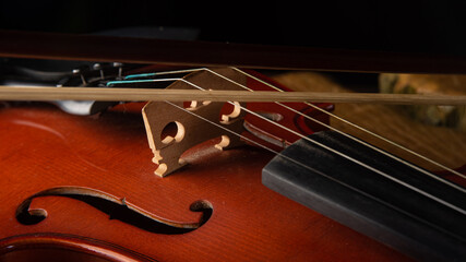 Details of an old and beautiful violin on a rustic wooden surface and black background, low key portrait, selective focus.