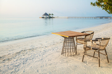 Wooden table and chairs on tropical beach by the water in tropical seashore in early morning, candid light