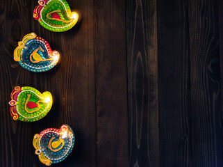 Top view overhead clay lit light a fire already on Diya or oil lamp, studio shot on black wooden background, Decoration of Hinduism rangoli, Happy celebration Deepavali or Diwali festival concept