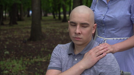 A woman puts her hand on the shoulder of a young man with cancer in support. The man puts his hand on the woman's hand. Hair loss due to chemotherapy.