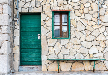 The green door, a window and a bench on the wall of sandstone
