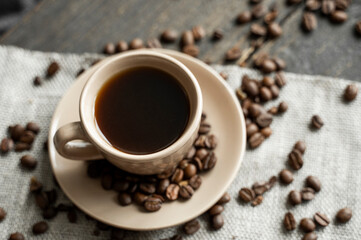 Coffee cup with roasted coffee beans on wooden table background. Mug of black coffe with scattered coffee beans on a wooden table. Fresh coffee beans.
