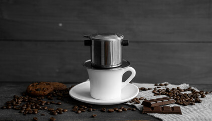 White cup of coffee with a metal filter on a top and scattered beans on a wooden table. Traditional vietnamese coffee.