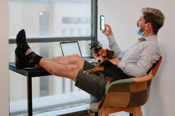 Businessman teleworking comfortably from his home, wearing socks and shorts, with his dog by his side.
