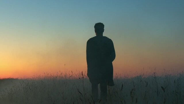 Silhouette of a man walking through a misty field during summer sunset