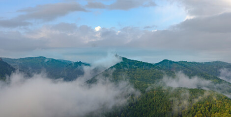 Fog in the mountains. Green and yellow forest on the mountain slopes. Wet fog in the valley. Sky with clouds. Takmak mountain in park Krasnoyarsk pillars. Natural blur.