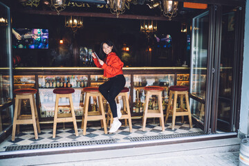Cheerful young ethnic woman relaxing at counter of street bar