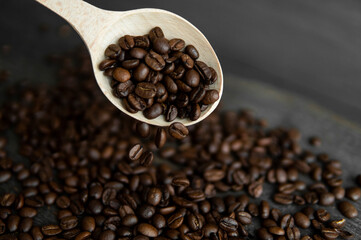 Fresh roasted arabica coffee beans falling from a oaken spoon on a wooden table.