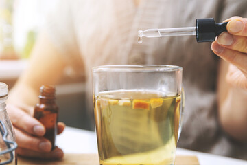 dietary supplements and vitamins - woman adding drops in cup of tea with dropper.