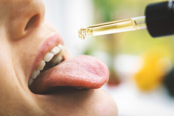 herbal alternative medicine and dietary supplements - woman taking cbd hemp oil drops in mouth from...