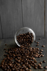 Roasted fresh arabica coffee beans scattered on a table from a little jar on a wooden table. Fresh coffee beans.