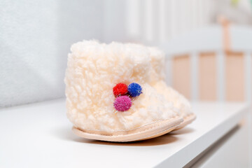 A pair of white wool baby booties are on the dresser. Close up. Nobody