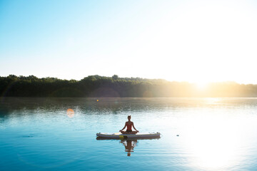 Fototapeta na wymiar Woman meditating and practising yoga during sunrise in paddle board