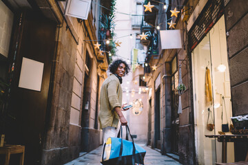 Obraz na płótnie Canvas Joyful ethnic man with bag strolling on street