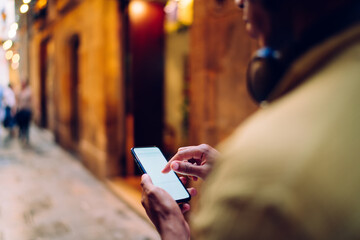 Crop man with headphones using cellphone on street