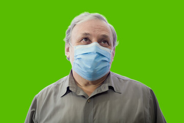 Portrait of a man in a shirt and medical mask looking up, isolated on a green background