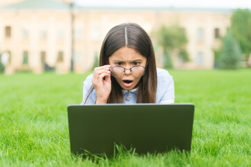 Oh no. back to school. teen girl use computer on green grass in park. child in glasses with notebook. new technology in modern life. study. surprised kid working on laptop. online education