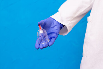 Jars for hijama bloodletting in the hands of a doctor in a white medical coat on a blue background....