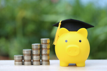Graduation hat on yellow piggy bank with stack of coins money on nature green background, Saving money for education concept