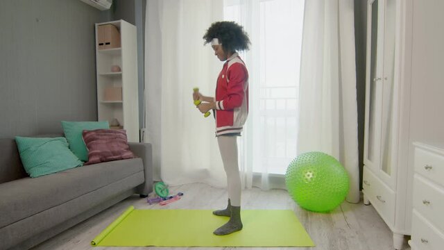 Young african american woman hippy in colourful sportswear with curly afro hairs is lifting green dumbels