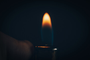 Hand holding a burning lighter in the dark, macro photo. Background with fire