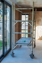 Property extension renovation, plastering of the walls, undercoat layer, scaffold tower in front. Unfinished walls and ceilings, selective focus