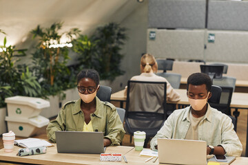 Portrait of two young African-American people wearing masks while working at desk in post pandemic...