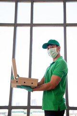 Green uniform delivery man wearing surgical mask and glove deliver  pizza package