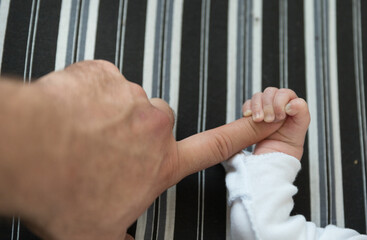 A little caucasian baby holding the finger of his father