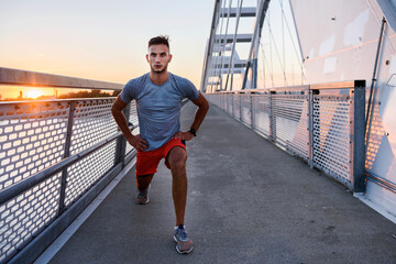 Young handsome sporty jogger taking break from exercising outdoors in the sunset