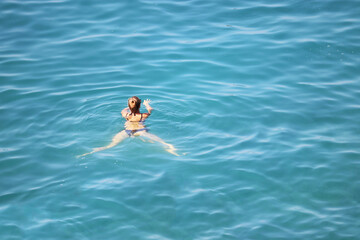 Woman in bikini swimming in the blue sea, aerial view. Relaxation on the water, beach vacations