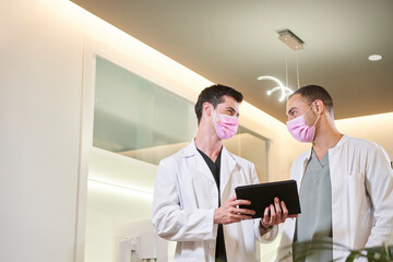 Two doctors with a mask commenting on results with a tablet in hand.
